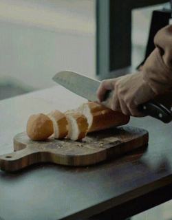 Close-up short looping video of someone slicing a baguette on a bread board
